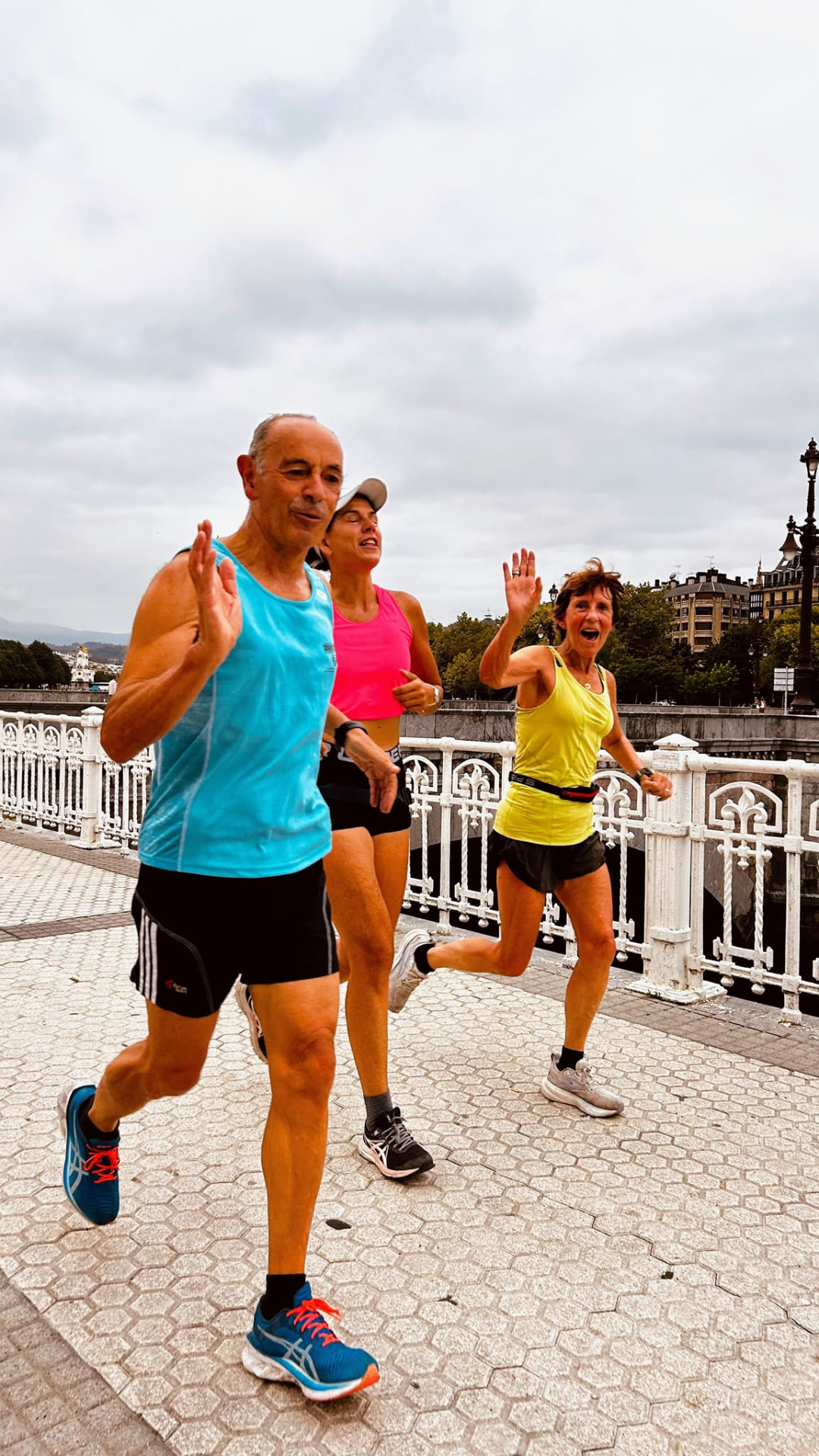 Three friends running together along a city promenade, smiling and waving